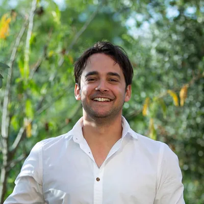 Portrait de Guillaume, souriant, en chemise blanche dans la nature.