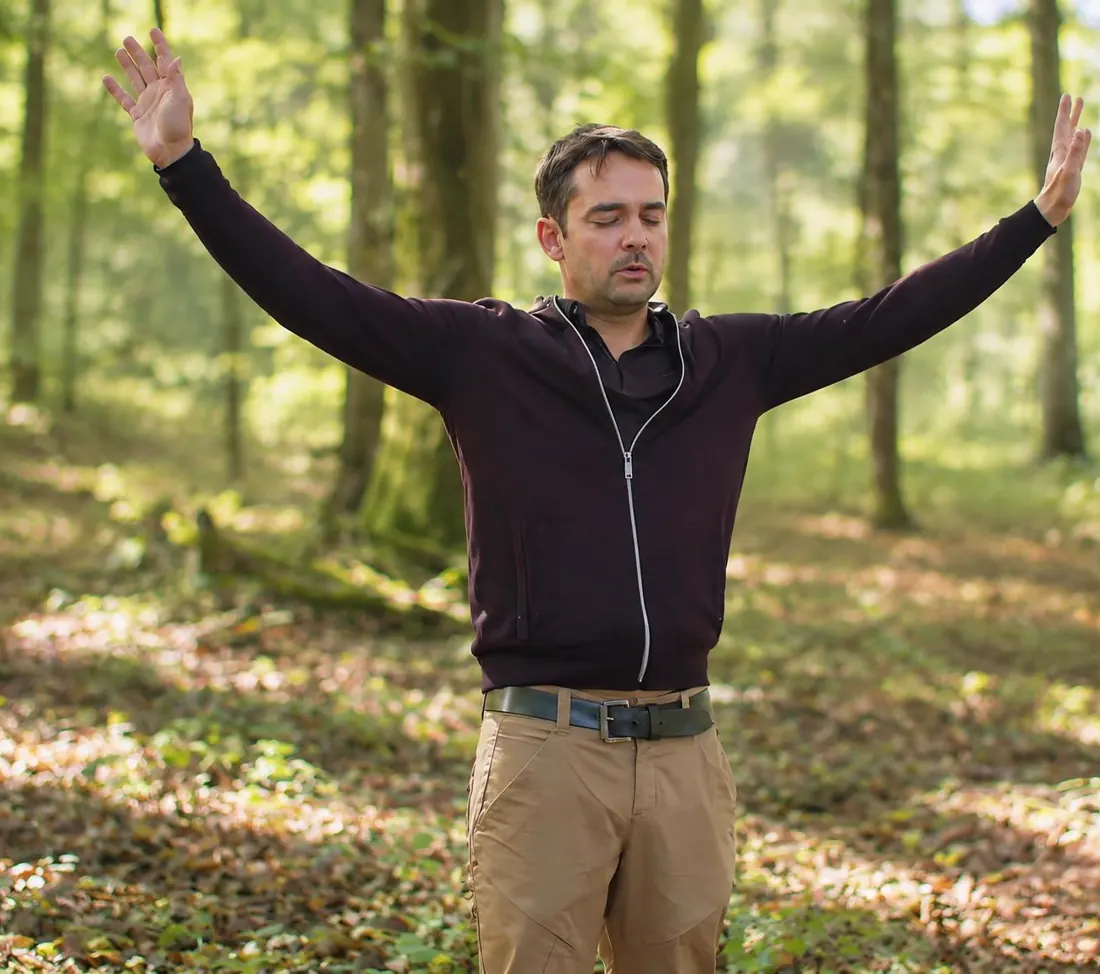 Guillaume en forêt, les bras grands ouverts, le visage apaisé.