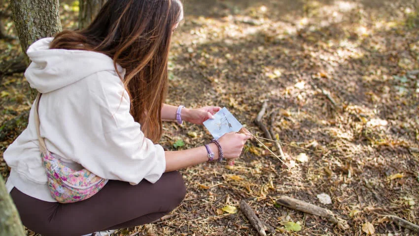 Une participante accroupie en forêt observe une carte, à l'écoute de ses ressentis.
